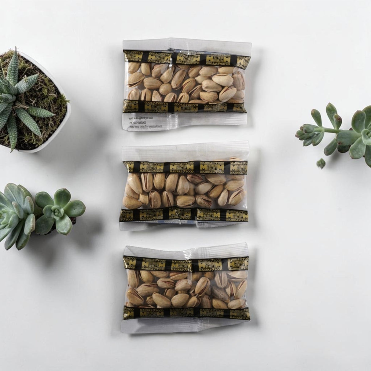 Three Mahnaz Food mini packs of premium Iranian pistachios in clear plastic pouches on a white surface with succulents.