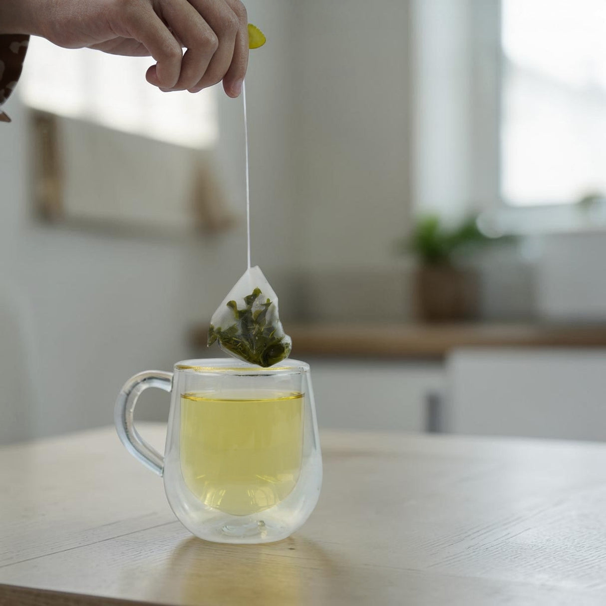 Mahnaz Food Moringa Herbal Tea Bag being steeped in a clear double-walled mug filled with golden tea.