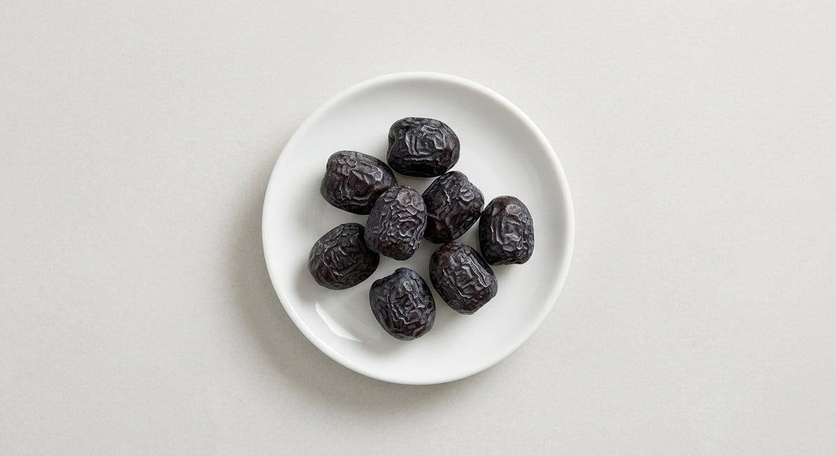 Small dark Ajwa dates arranged on a plain white dish