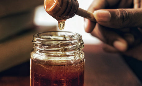 Tangan memegang gayung madu yang penuh dengan madu, kaya dengan khasiat madu lebah.