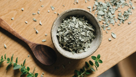 Bowl of dried marjoram leaves with fresh marjoram sprigs on a wooden table