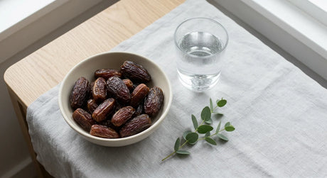 Bowl of dates and a glass of water on a table in soft natural light