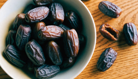 Bowl of dark oval Safawi dates with soft wrinkled skin on a wooden table