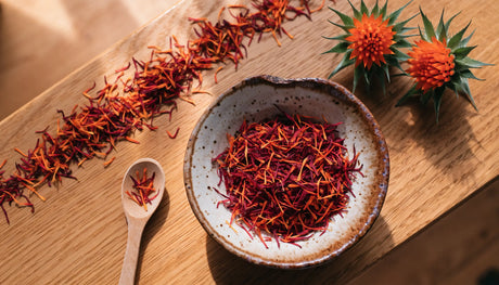 Bowl of dried orange-red safflower petals beside fresh safflower blossoms