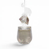 Mahnaz Food Rose Tea sachet steeping in a clear glass of hot tea, releasing steam.