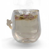 Mahnaz Food Rose Tea, loose dried rose petals steeped in clear hot water in a double-walled glass mug with butterfly handle.