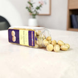 Mahnaz Food premium macadamia nuts in a clear plastic jar, spilled out on a white background.