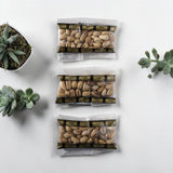 Three Mahnaz Food mini packs of premium Iranian pistachios in clear plastic pouches on a white surface with succulents.