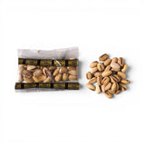 Mahnaz Food premium Iranian pistachios in a 30g mini pack next to a pile of roasted, shell-on nuts.