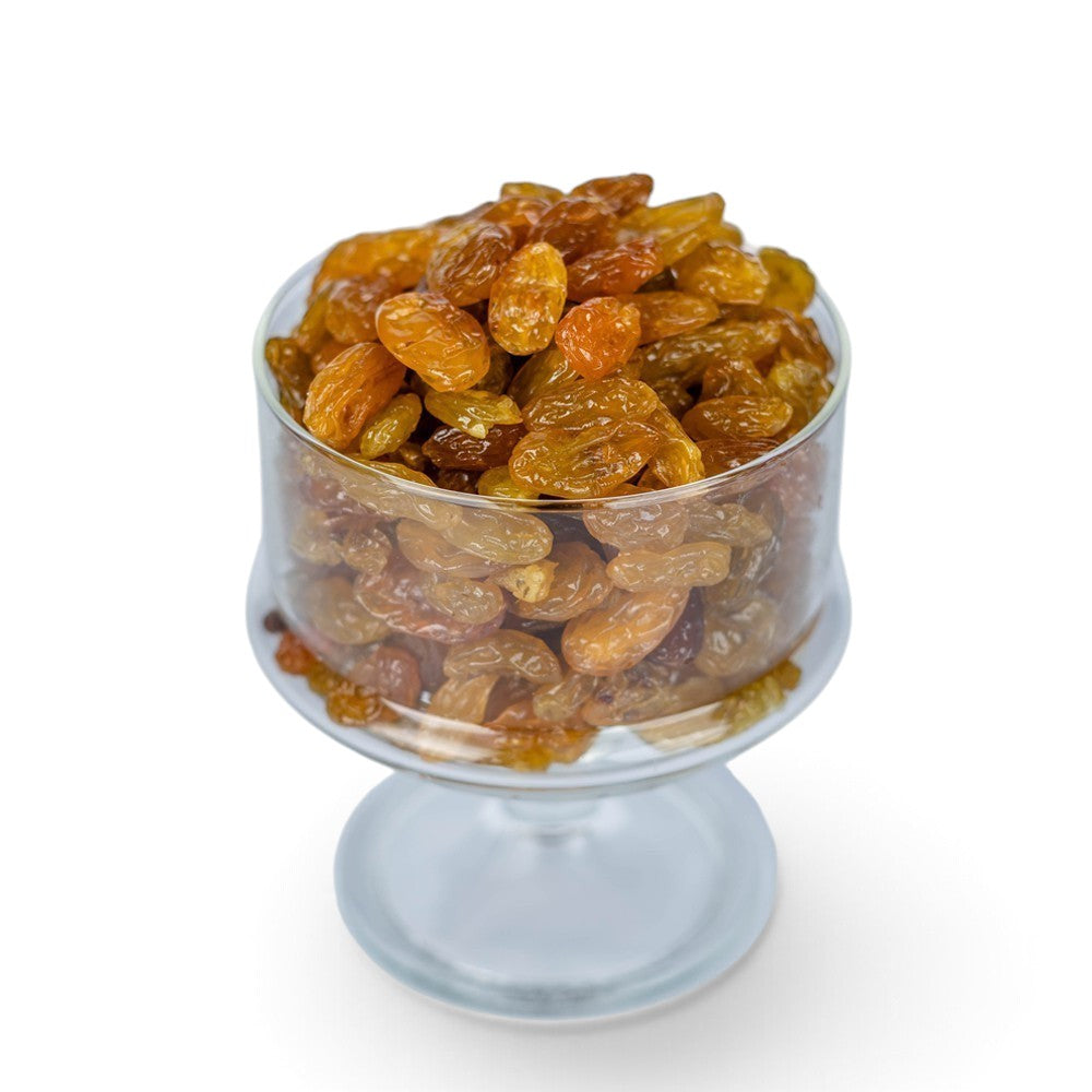 Mahnaz Food golden jumbo raisins piled in a clear glass pedestal bowl against a white background.