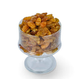 Mahnaz Food golden jumbo raisins piled in a clear glass pedestal bowl against a white background.