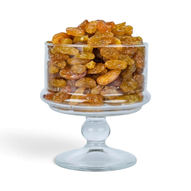 Mahnaz Food golden jumbo raisins piled high in a clear glass pedestal bowl against a white background