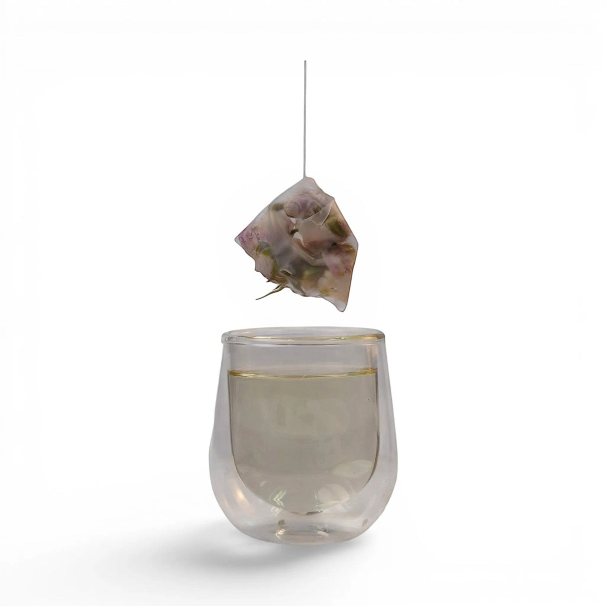 Mahnaz Food Herbal Memory Tea bag with rose petals, saffron & cardamom, steeping in a clear glass.
