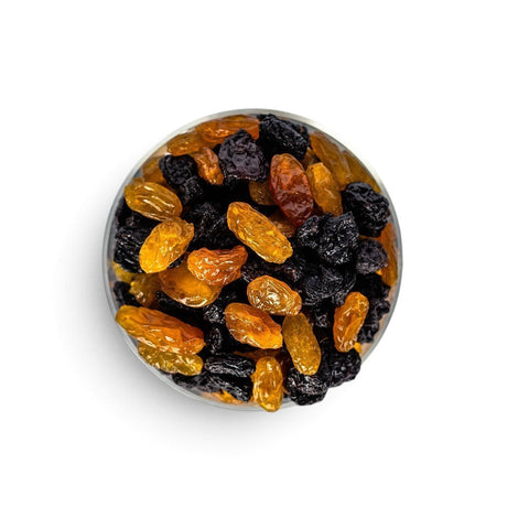 Mahnaz Food jumbo black and golden raisins mixed in a glass bowl, top-down view on a white background.