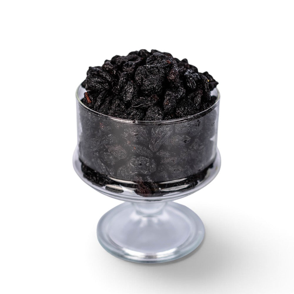 Mahnaz Food jumbo black raisins served in a clear glass pedestal bowl against a white background