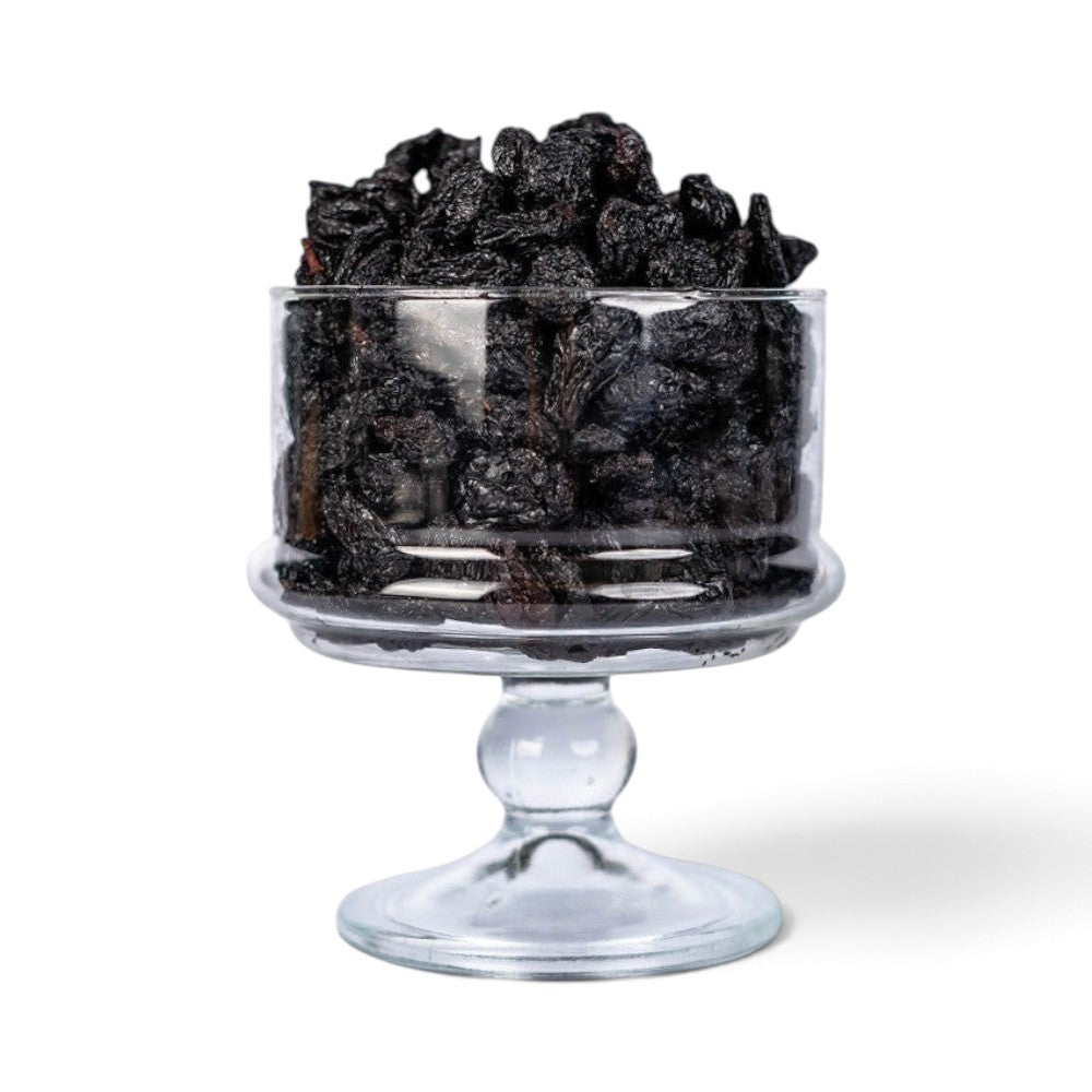Mahnaz Food jumbo black raisins piled high in a clear glass pedestal bowl against a white background