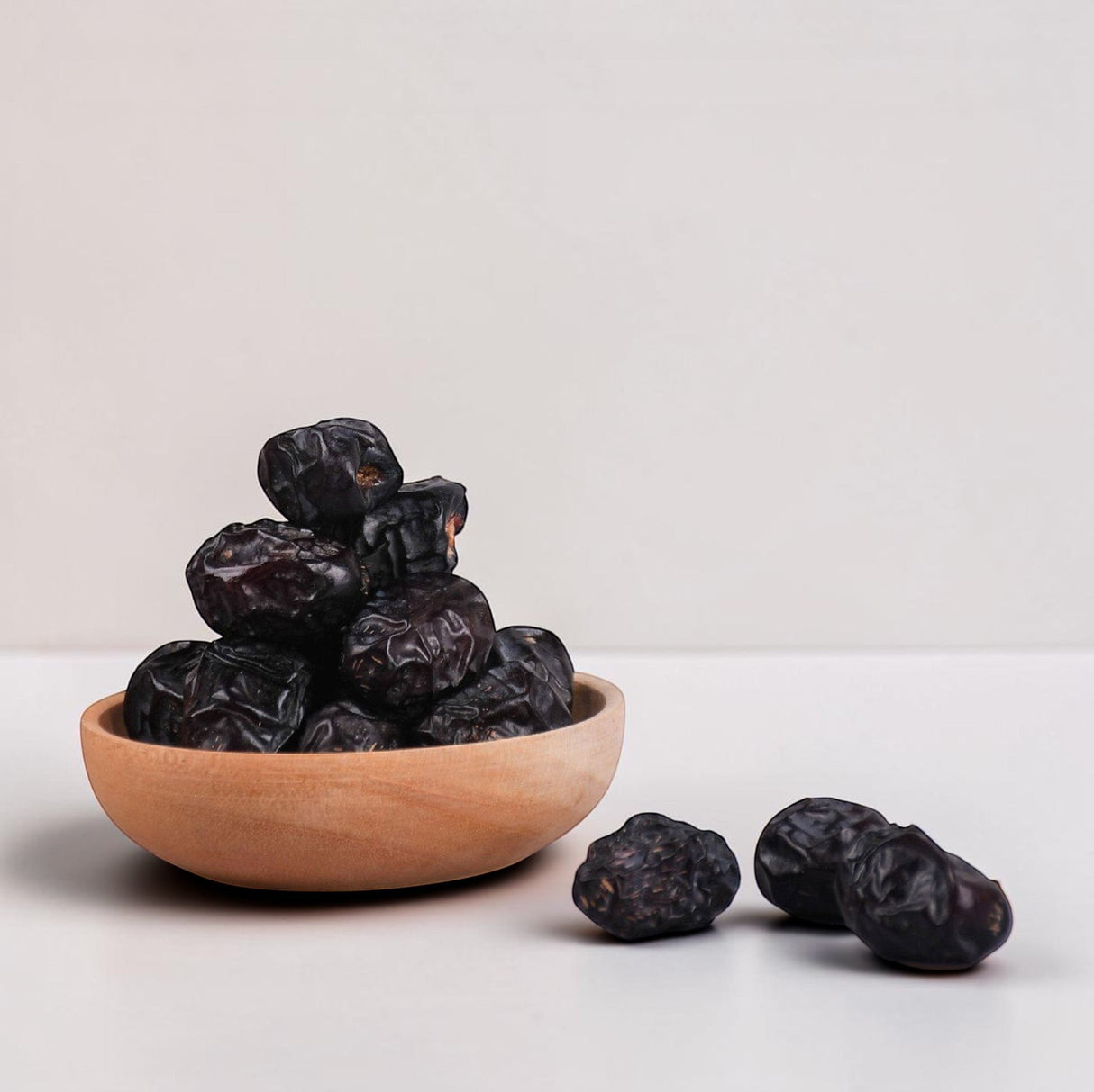 Mahnaz Food Madinah Ajwa dates are dark brown, soft, and wrinkled, served in a wooden bowl.