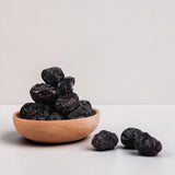 Mahnaz Food Madinah Ajwa dates are dark brown, soft, and wrinkled, served in a wooden bowl.