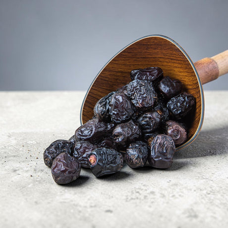 Mahnaz Food Madinah Ajwa dates are dark brown, wrinkled, and soft, served in a wooden scoop.
