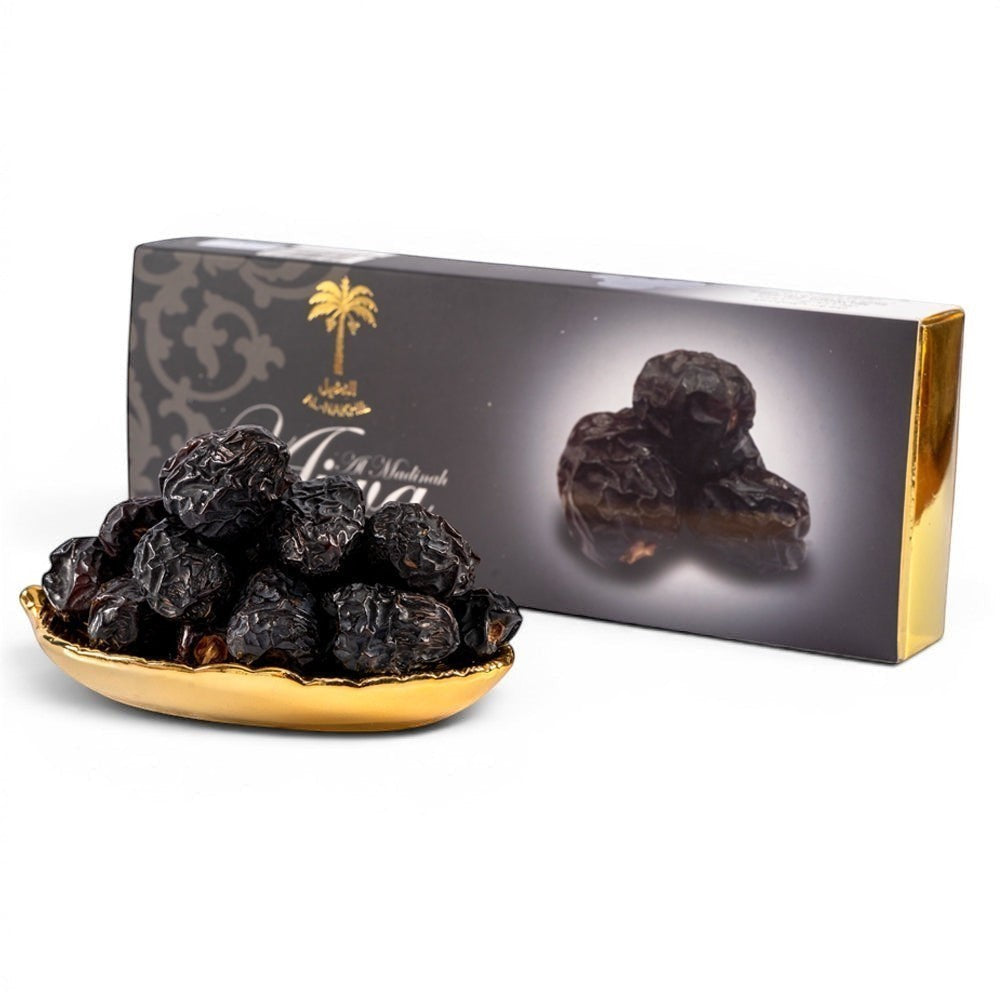 Mahnaz Food Madinah Ajwa dates, dark brown to black, soft and dry, presented in a golden dish with a premium packaging box.