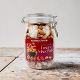 Mahnaz Food premium mixed nuts in a clear glass jar with a metal latch lid, featuring assorted roasted nuts.