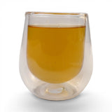 Mahnaz Food Royal Green Tea loose leaf in a double-walled glass cup, golden amber color, 120g pack.