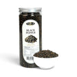 Mahnaz Food premium whole black peppercorns in a clear plastic jar next to a small white bowl filled with peppercorns